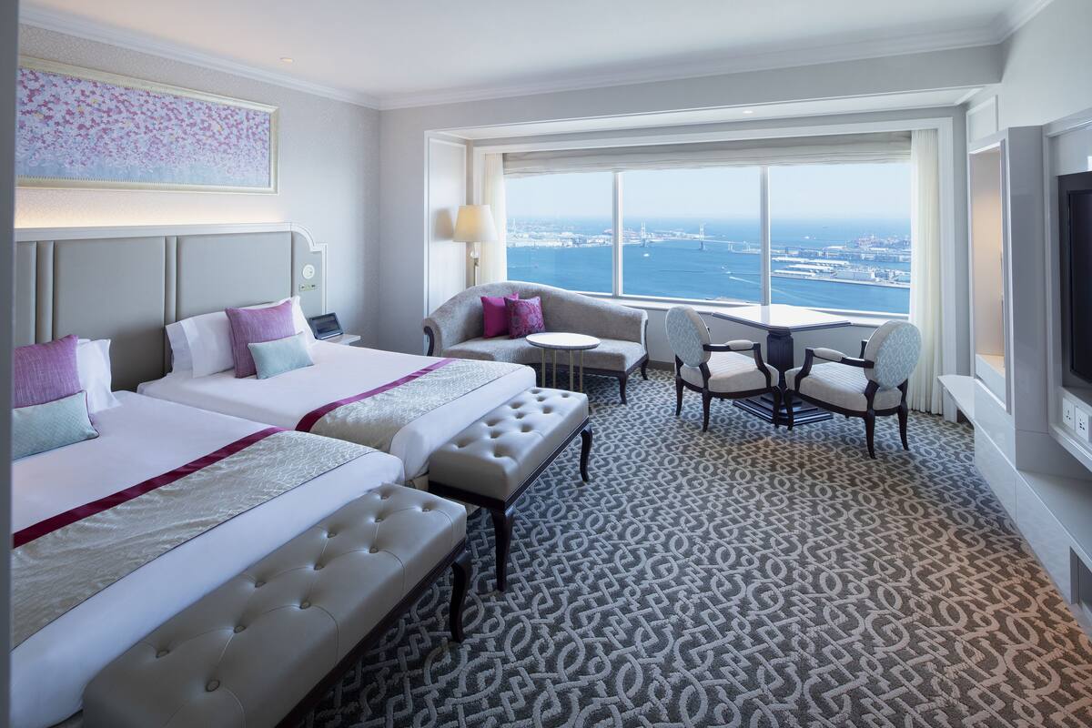 A hotel room with two beds, a sofa, a small table, and a TV.