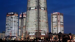 Un edificio alto con varios pisos y ventanas, rodeado de otros edificios y una masa de agua.