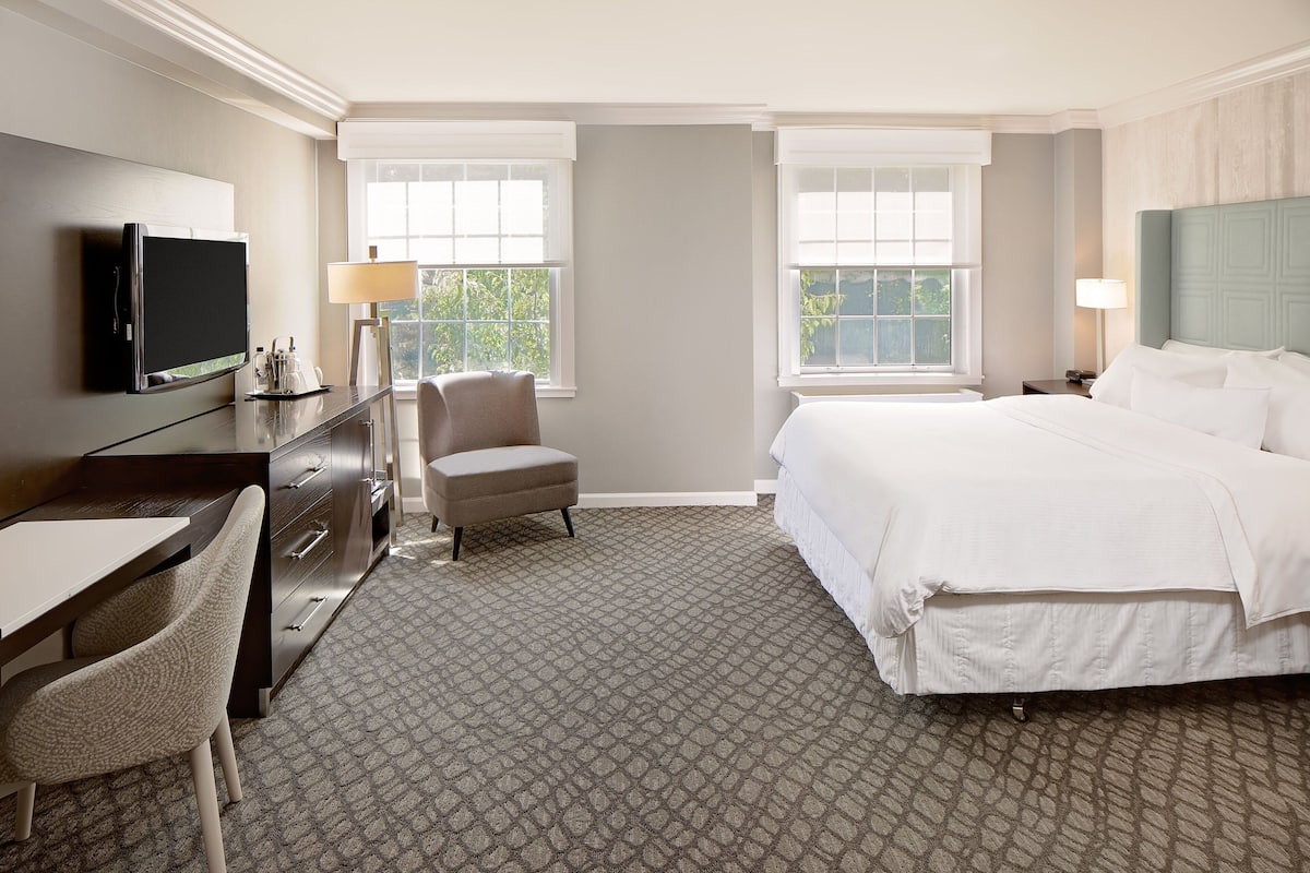 A hotel room with a bed, a desk with a computer, a chair, and two windows.