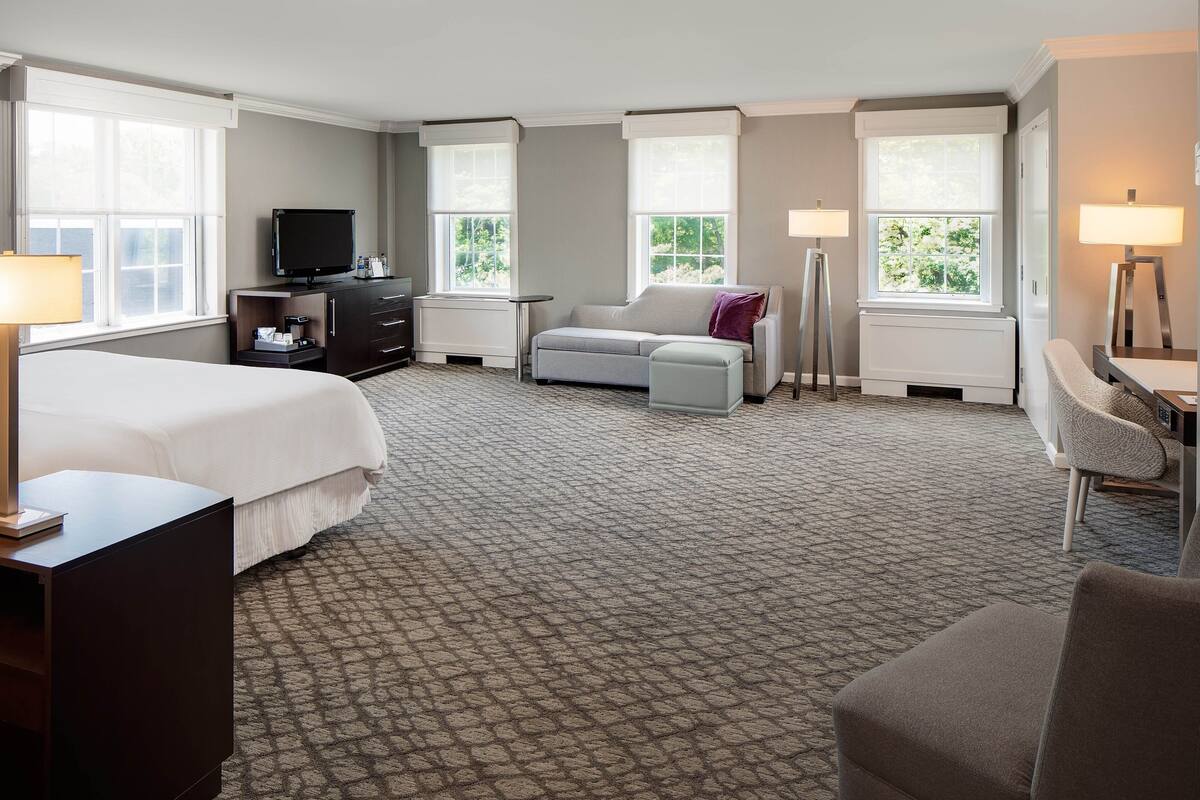 A hotel room with a large bed, a sofa, a desk, and a TV.