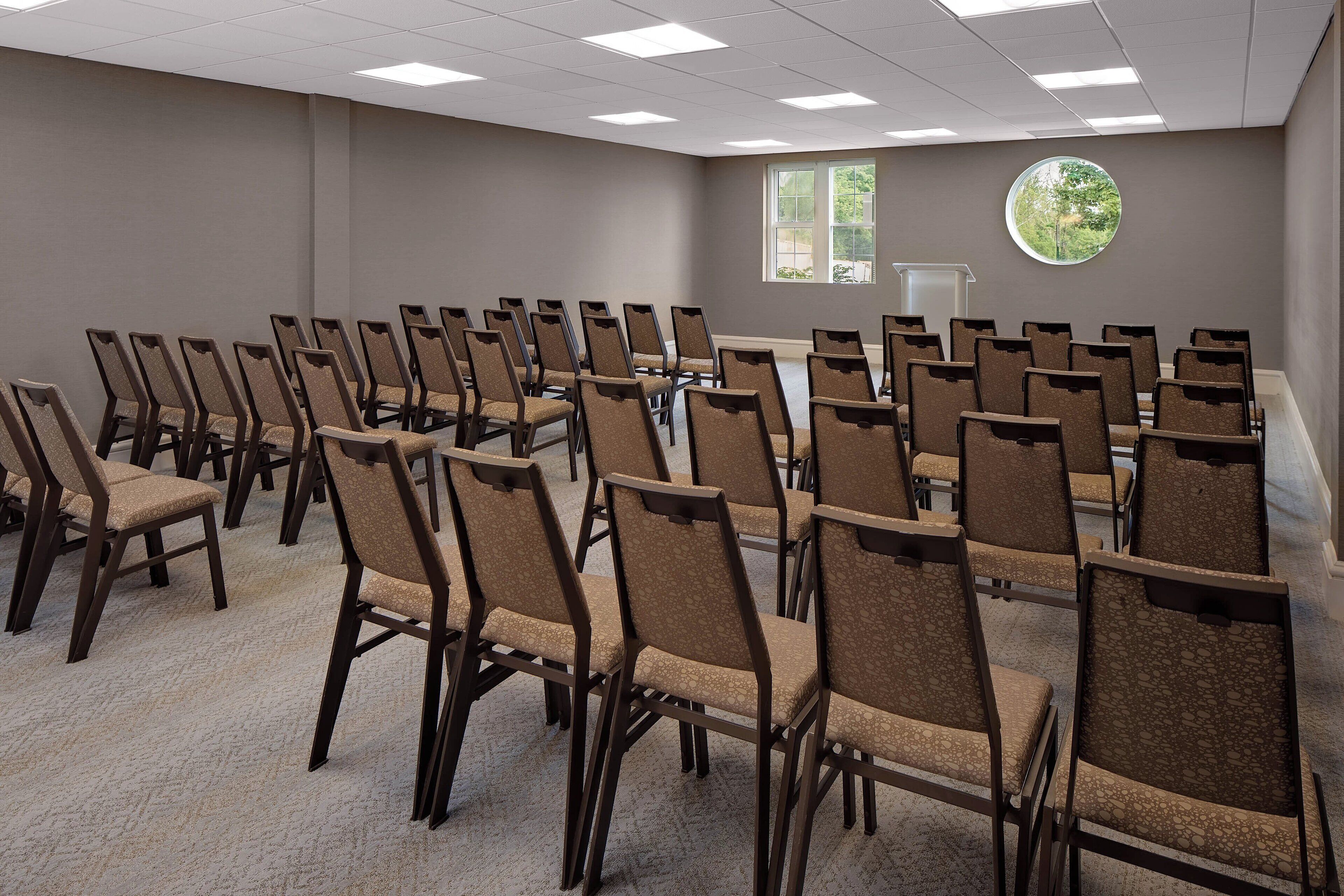 A conference room with rows of chairs, a podium, and a window with a view of greenery.