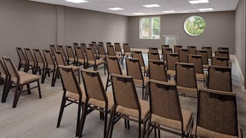 A conference room with rows of chairs, a podium, and a window with a view of greenery.