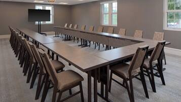 Une salle de conférence avec une longue table et des chaises, un téléviseur à écran plat et des fenêtres.