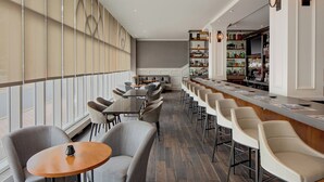 A modern bar area with a long counter, multiple seating options including bar stools and tables, and a large wine rack in the background. - The Westin Governor Morris, Morristown (Morristown)