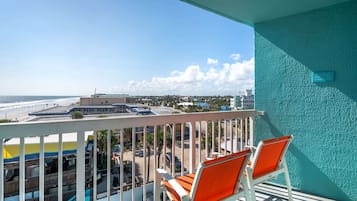 A balcony with two orange chairs, a view of the beach, and a sign indicating a restaurant.