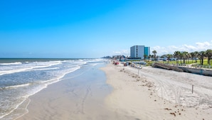 Ein Strand mit sandigem Ufer, blauem Himmel und einem Gebäude im Hintergrund.
