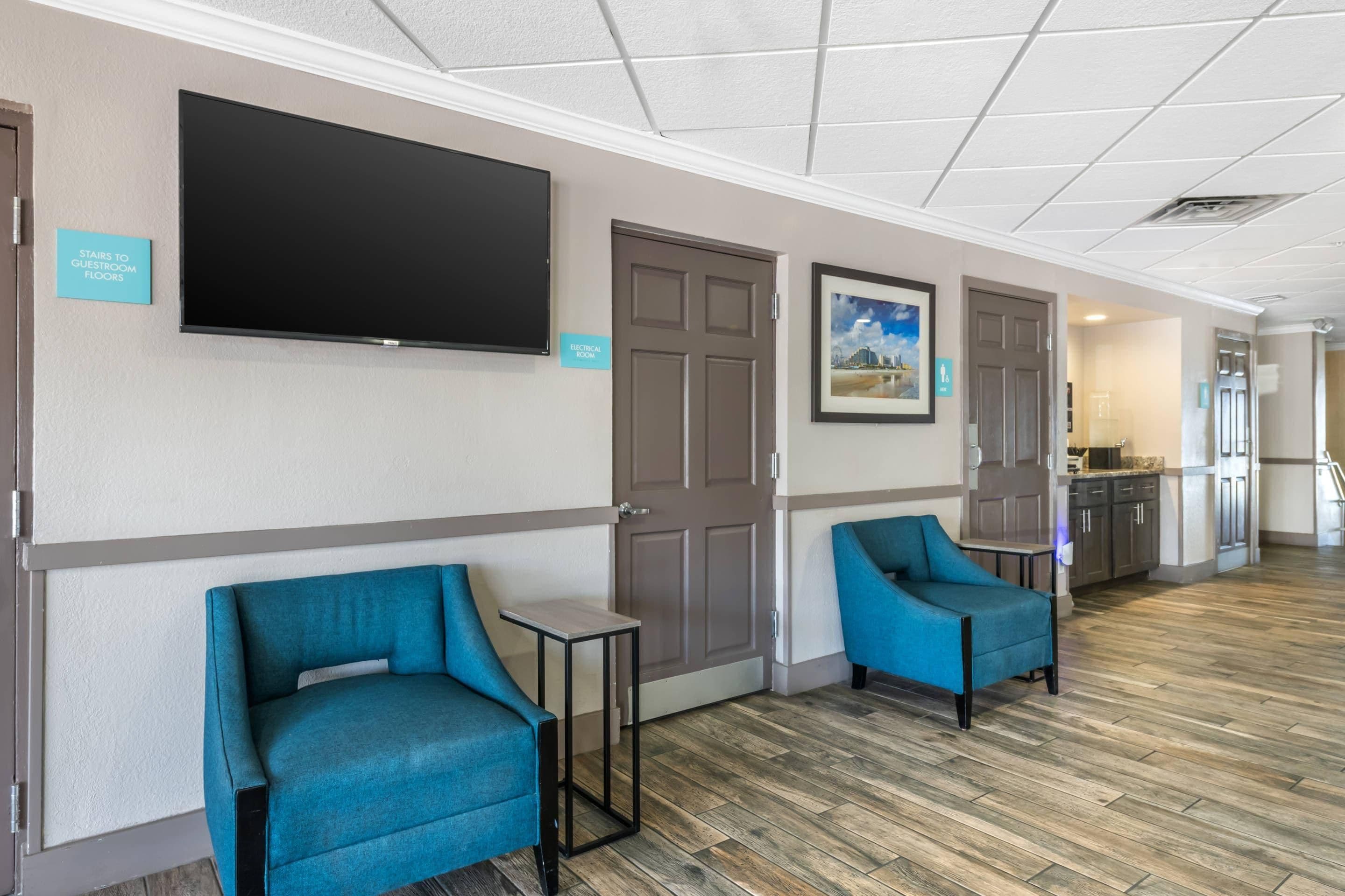 Un vestíbulo de hotel con un televisor de pantalla plana, dos sillones azules, una mesita y un cuadro en la pared.
