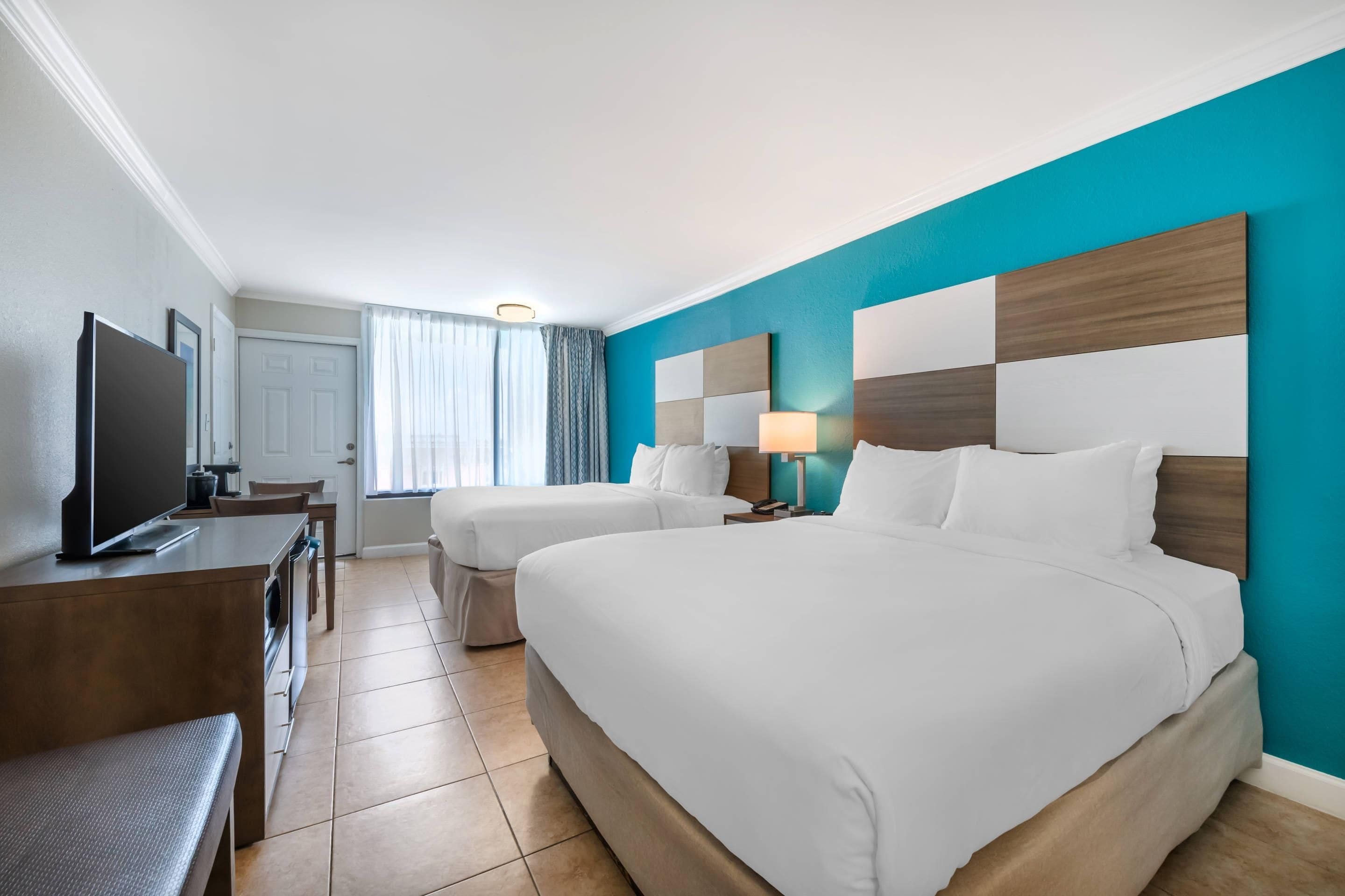 Habitación de hotel con dos camas, televisión, escritorio y ventana con cortinas.