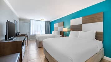 Habitación de hotel con dos camas, televisión, escritorio y ventana con cortinas.