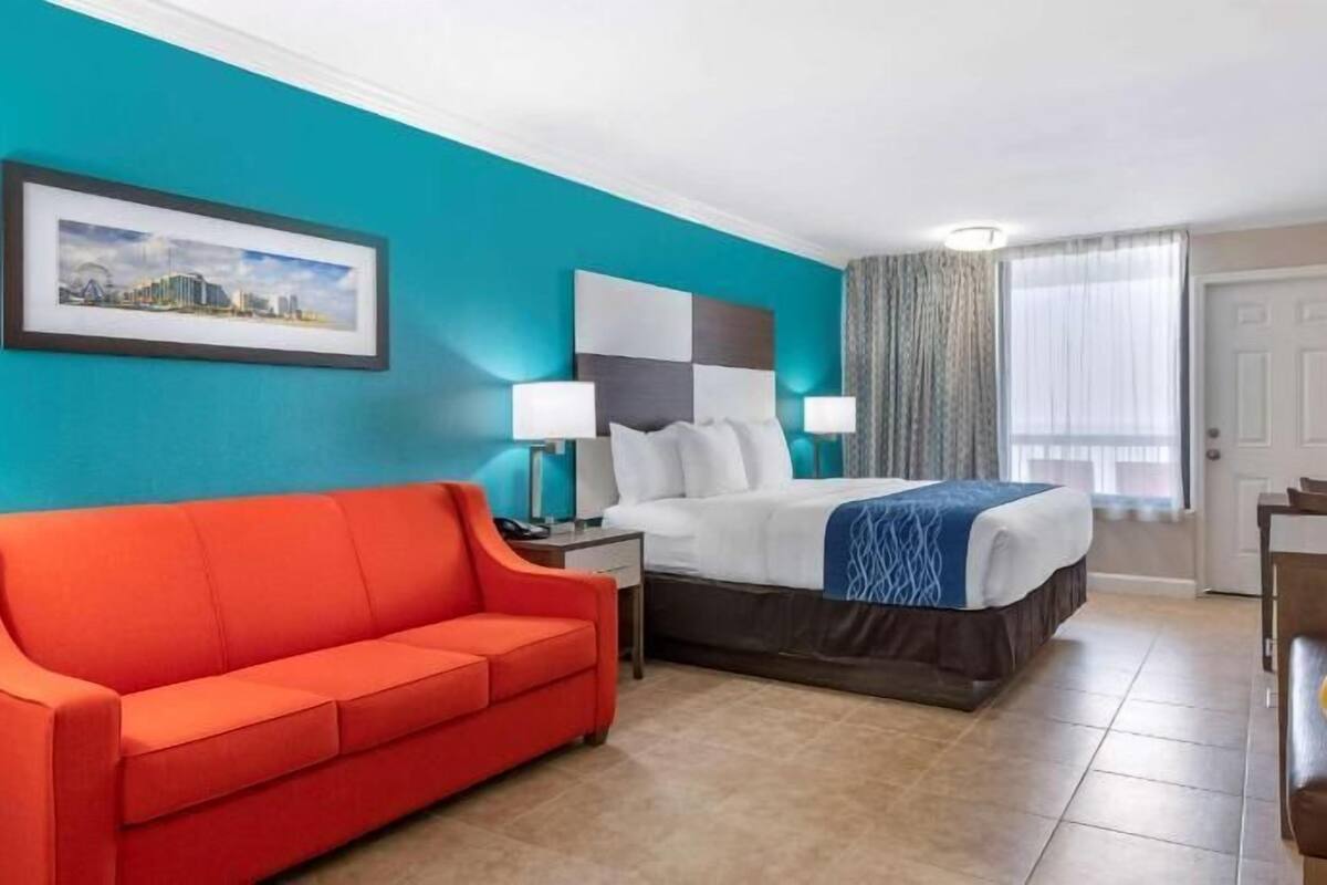 A hotel room with a bed, a red sofa, a TV, and a painting on the wall.