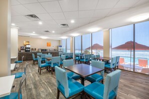 A restaurant with blue chairs and tables, a counter with a coffee machine, and large windows with a view of the ocean. - Comfort Inn & Suites Daytona Beach Oceanfront (Daytona Beach)