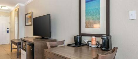 A compact hotel room with a kitchenette, a flat-screen TV, a framed landscape picture, and a coffee maker on the counter.