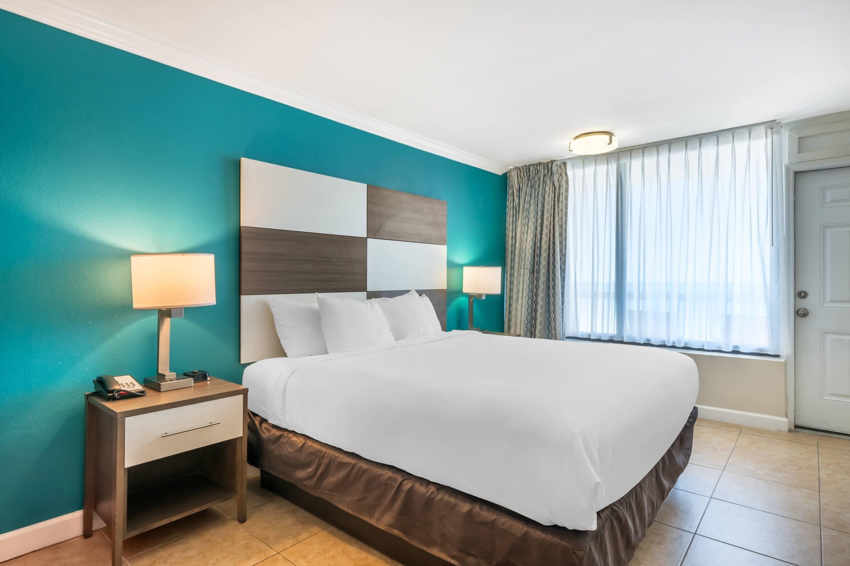 A hotel room with a bed, bedside lamps, a nightstand, and a window with curtains.