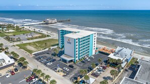 Ein Hotel mit großem Parkplatz, Blick auf den Strand und einem Pier im Hintergrund.