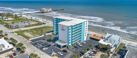 Un hotel con un amplio estacionamiento, vista al mar y un muelle al fondo.