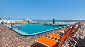 Ein Poolbereich mit Blick auf den Ozean, umgeben von orangefarbenen Liegestühlen und einer gefliesten Terrasse.