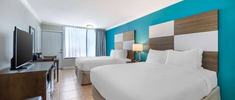 A hotel room with two beds, a TV, a desk, and a window with curtains.