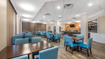 A hotel lobby with multiple seating areas, a reception desk, and a kitchen in the background.