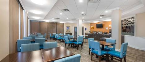 A hotel lobby with multiple seating areas, a reception desk, and a kitchen in the background.