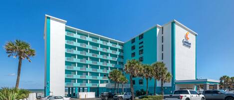 A multi-story hotel with a blue and white exterior, a parking lot, and palm trees.