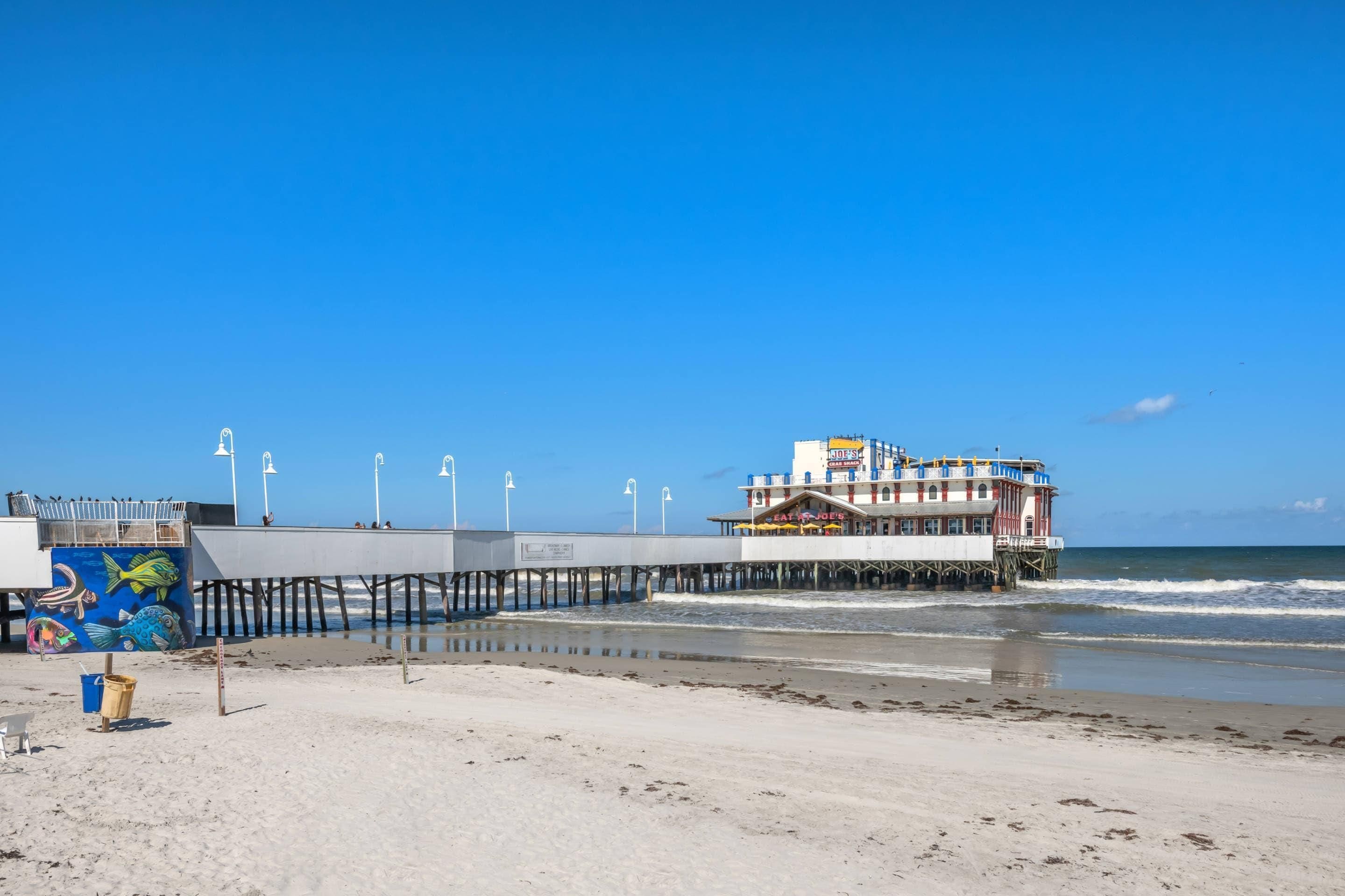 A pier extending into the ocean with a building featuring a sign for 'Joe's Crab Shack' and a mural of fish.