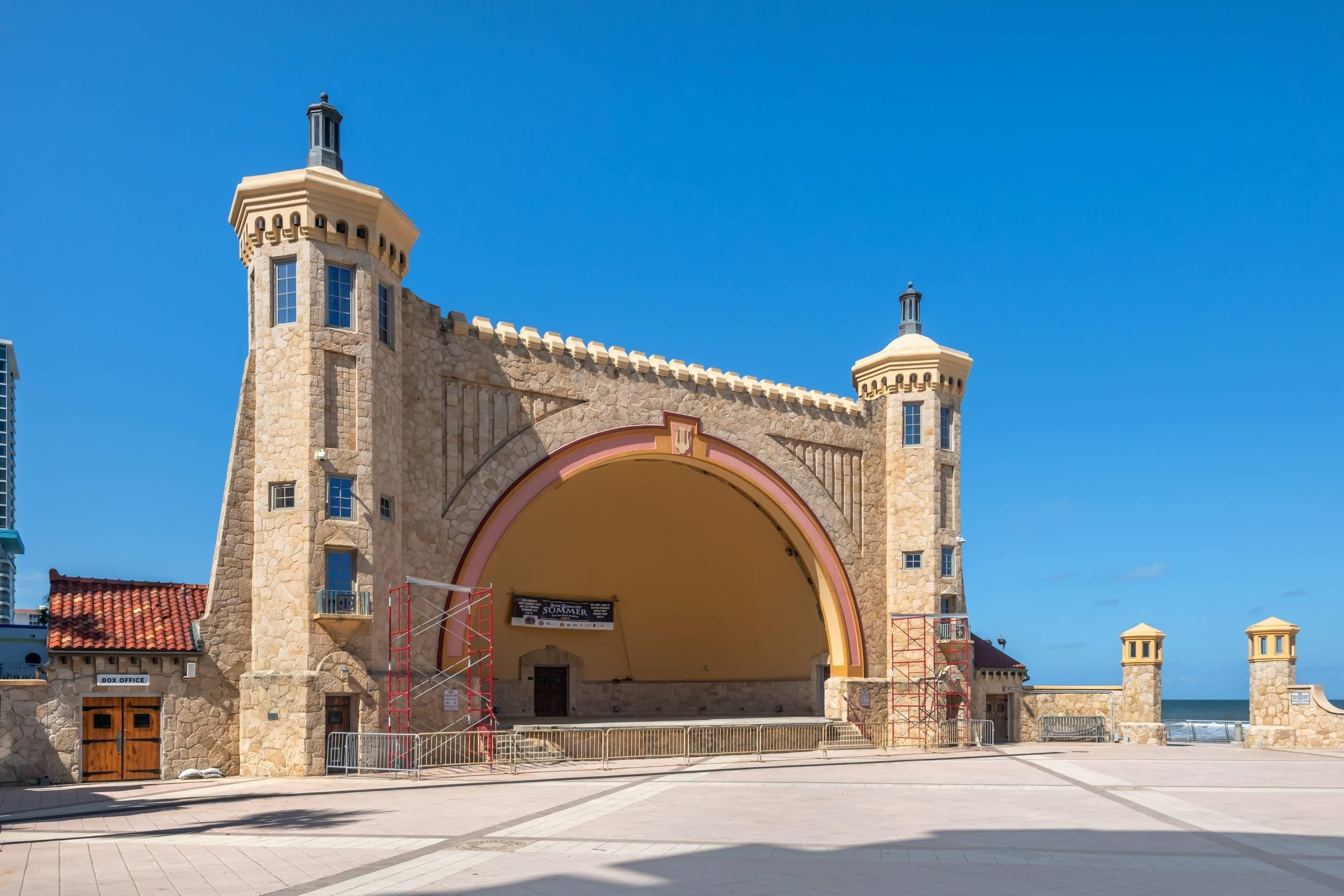 A historic stone building with a large arched entrance, two towers, and a sign indicating a summer event.