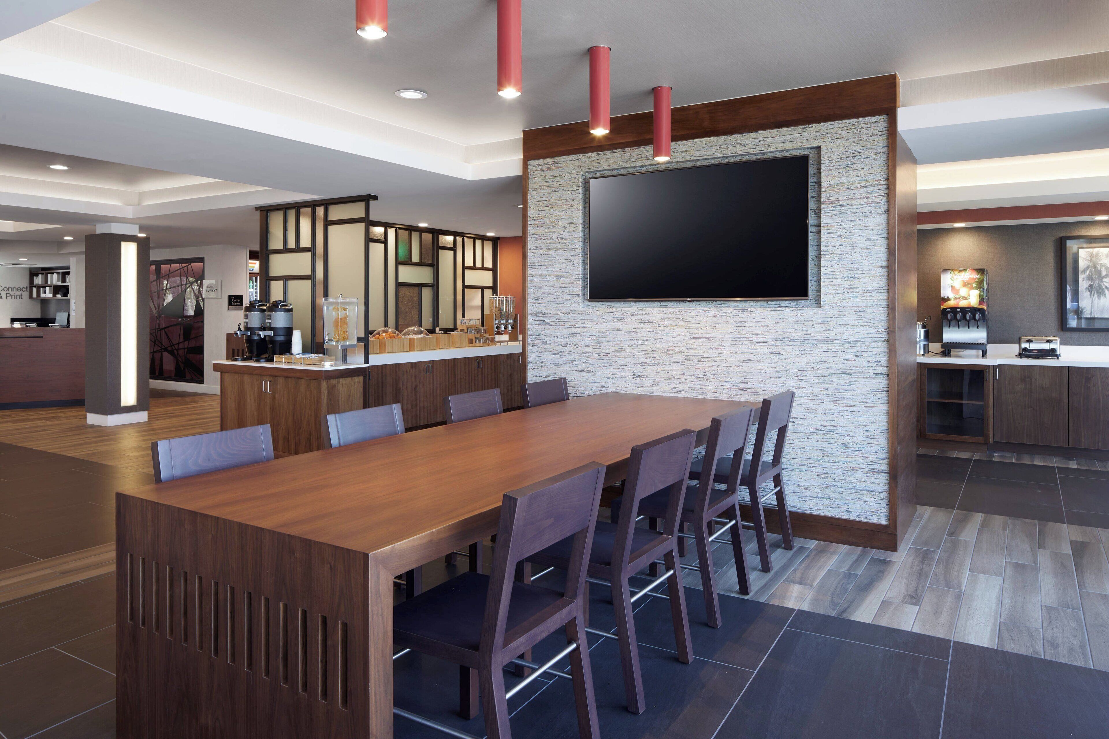 Uma cozinha moderna com uma ilha grande, uma área de refeições com mesa e cadeiras de madeira, e uma TV de tela plana fixada em uma parede texturizada.