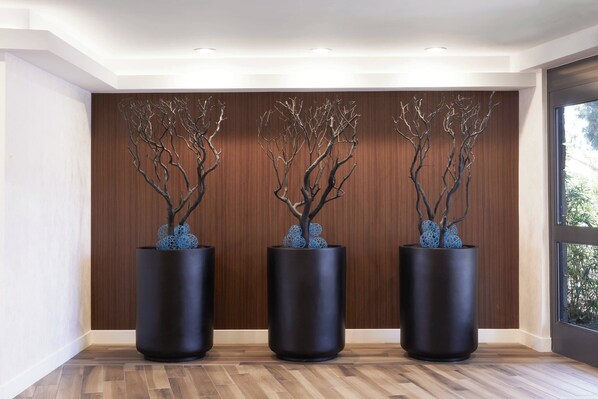 Three black cylindrical vases with branches and blue spherical ornaments on a wooden wall.
