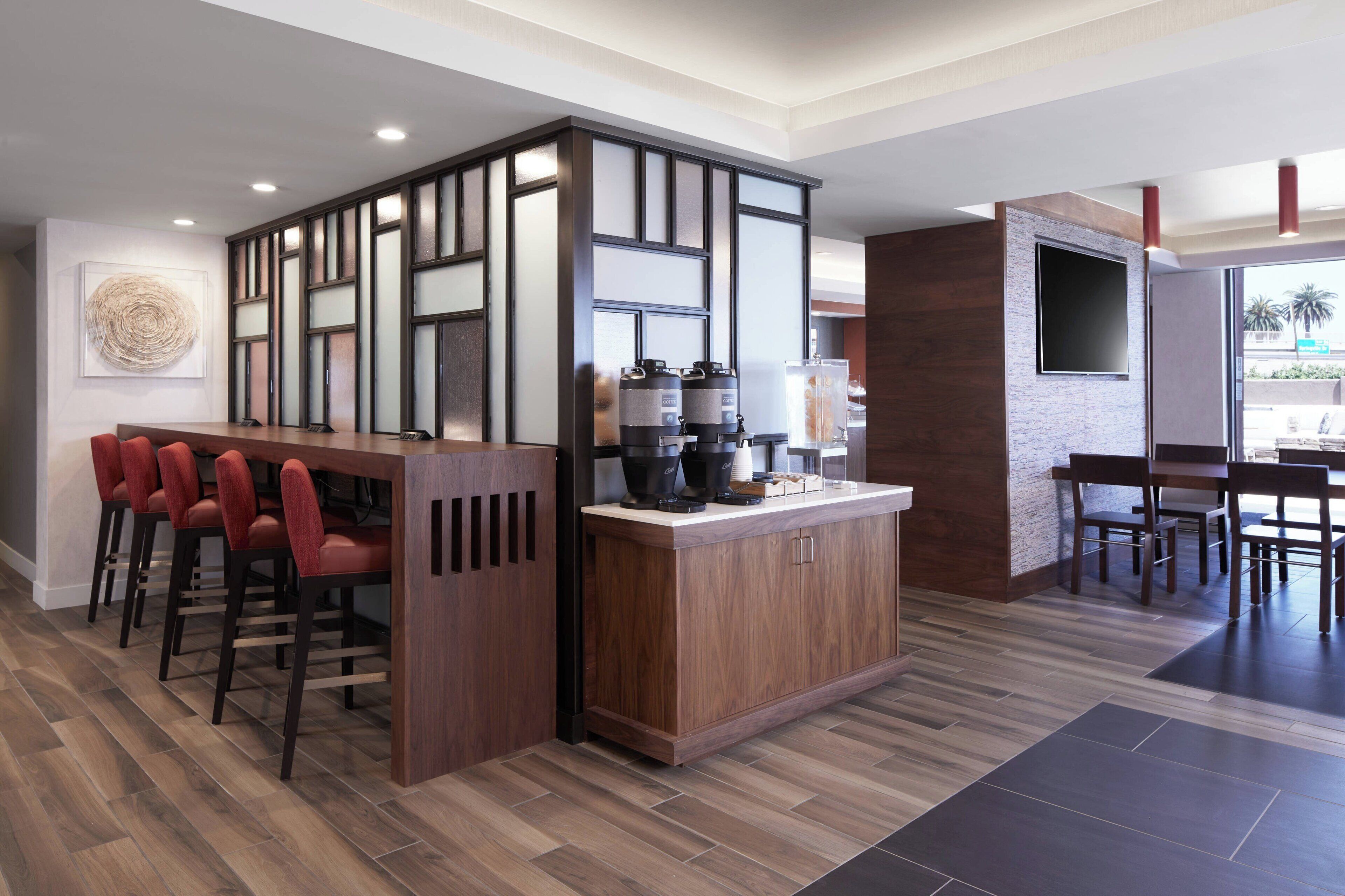 A modern bar area with a wooden counter, red bar stools, and a coffee machine.