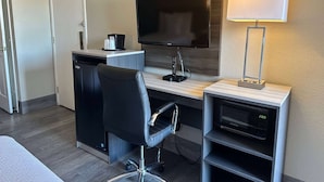 Habitación de hotel con escritorio, televisión de pantalla plana, microondas, silla y lámpara.