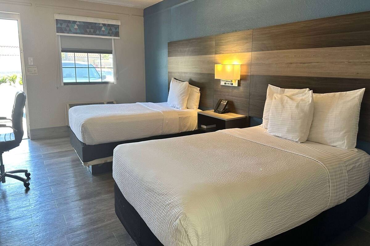 A hotel room with two beds, a desk, a chair, and a window with blinds.