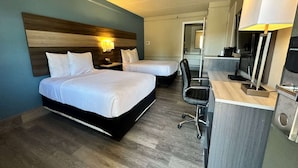 Una habitación de hotel con dos camas, un escritorio con una silla, un televisor y un espejo.