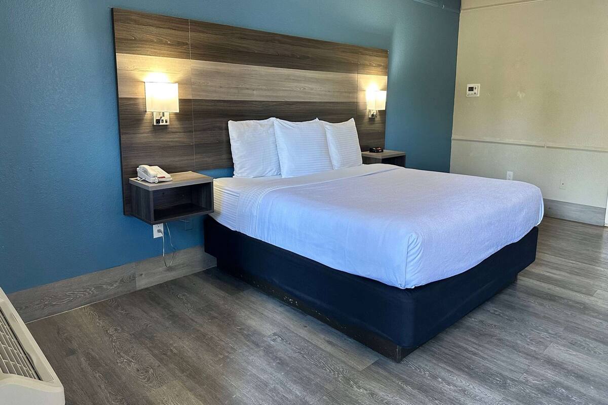 A hotel room with a large bed, two bedside tables, a wall-mounted lamp, and a thermostat.