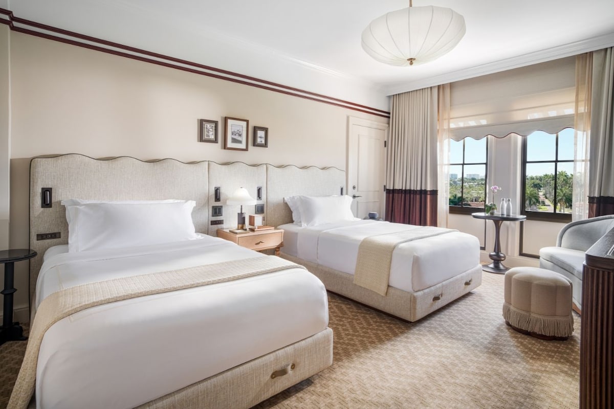 Habitación de hotel con dos camas, zona de estar y vistas al exterior.