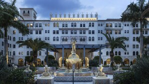 A grand hotel with a central fountain, multiple balconies, and lush greenery.