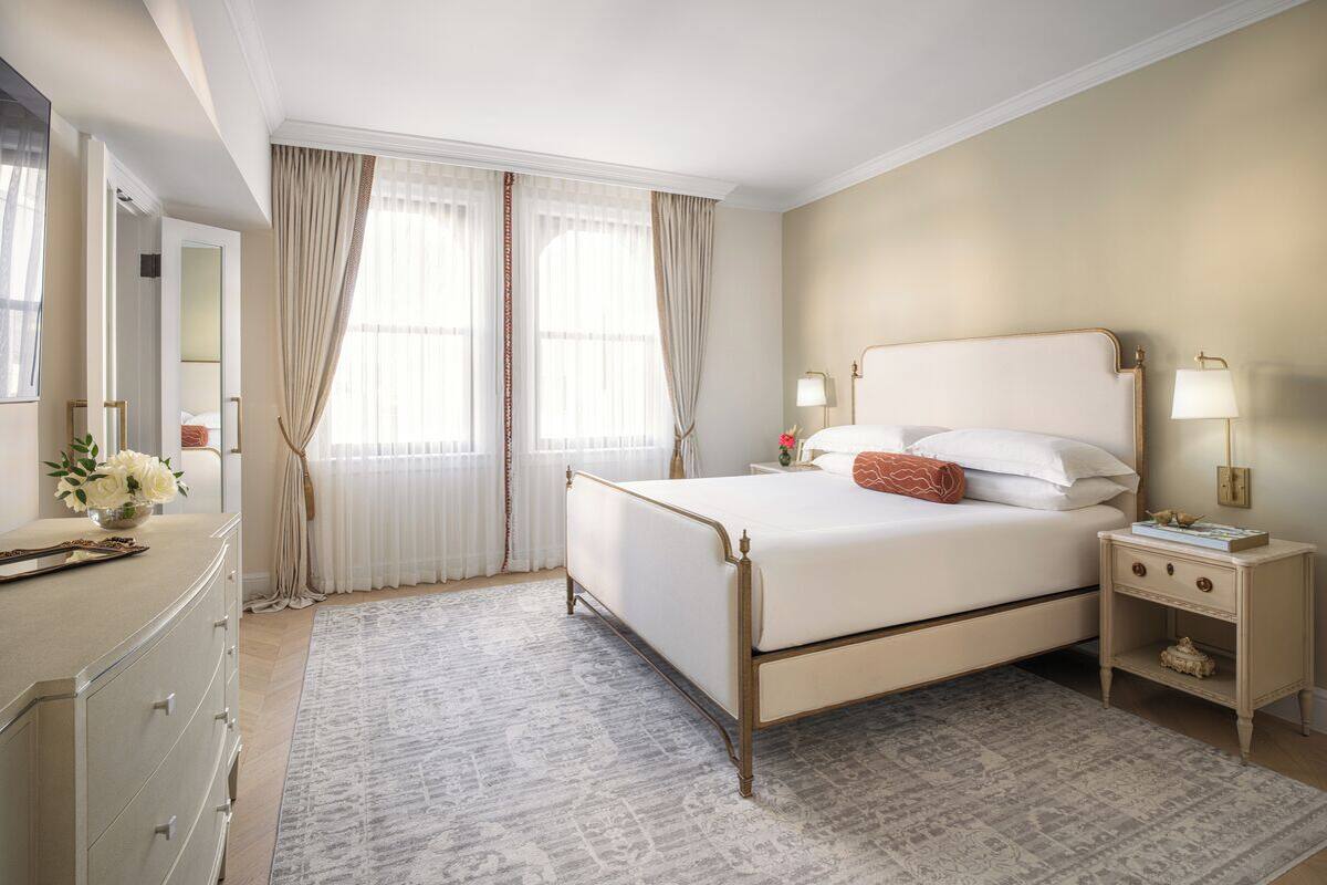 A hotel room with a large bed, bedside tables, a dresser, and a window with curtains.