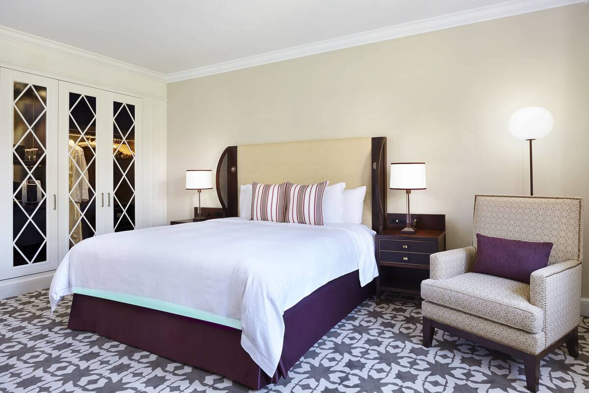 A hotel room with a large bed, a chair, a nightstand, and a wardrobe.