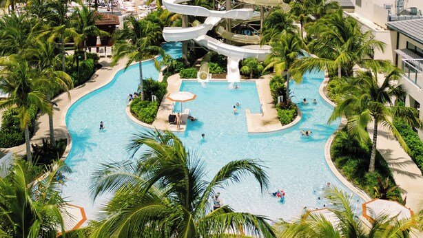 A large pool with multiple slides surrounded by palm trees and a view of the ocean.