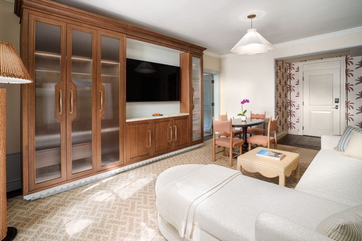Una sala de estar con un sofá, un televisor, una mesa de comedor con sillas y un mueble de madera grande con puertas de cristal.