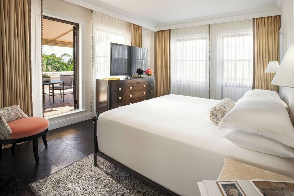 A hotel room with a large bed, a desk with a TV, a chair, and a view of the outdoors.