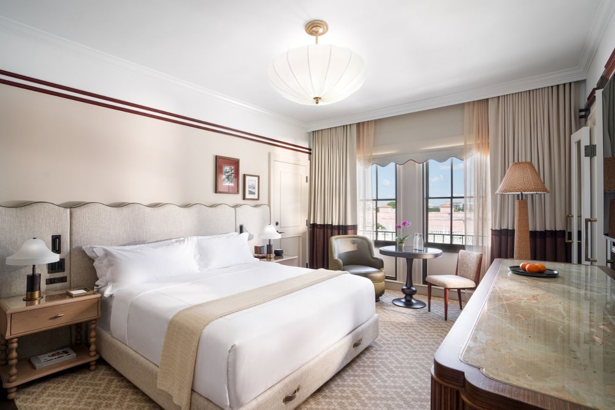 Habitación de hotel con una cama grande, un escritorio, dos sillas, una mesa redonda y vistas al exterior.