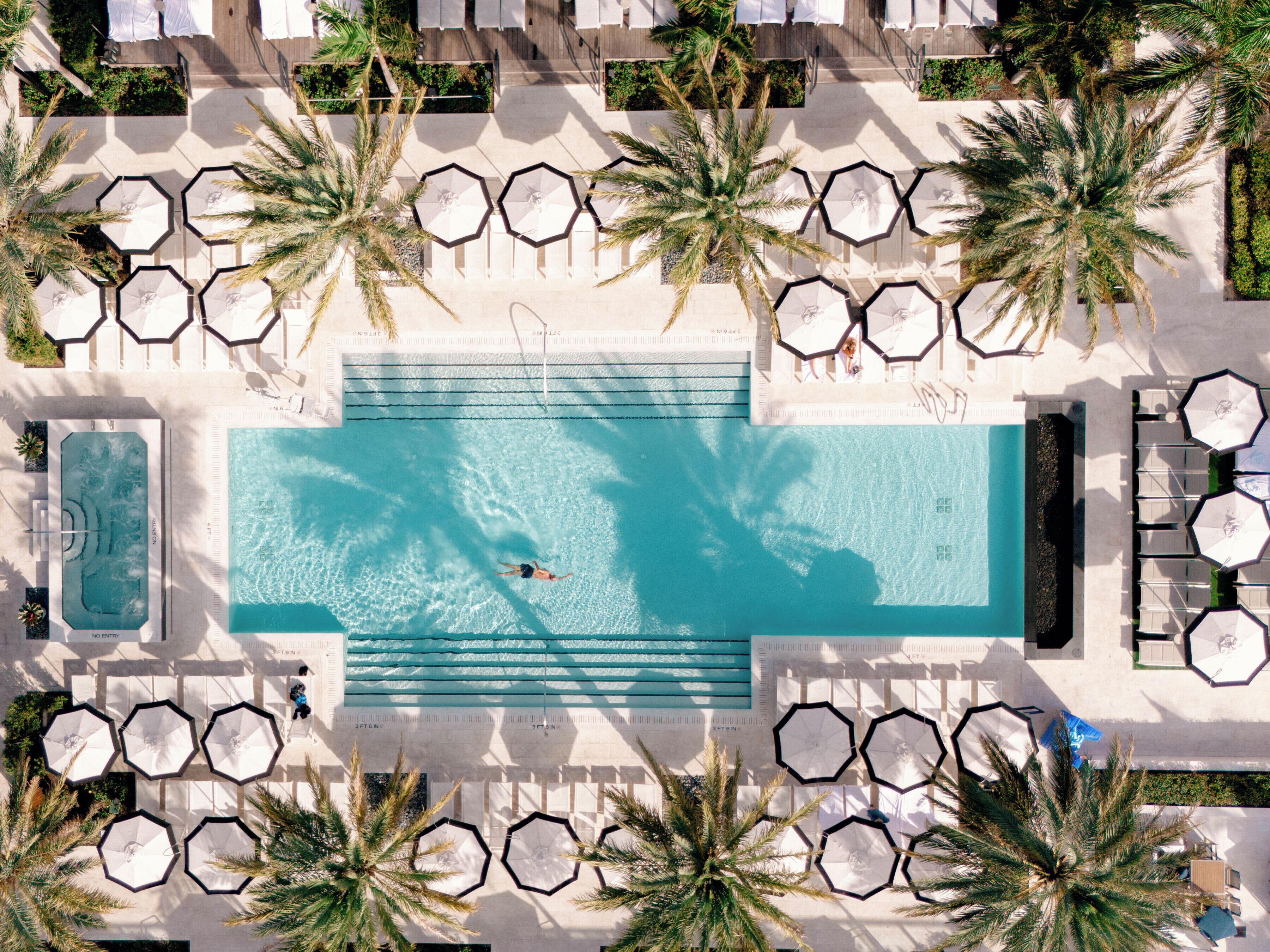 Vista aérea de un área de piscina en un resort, con sombrillas hexagonales, palmeras y sillas de descanso.