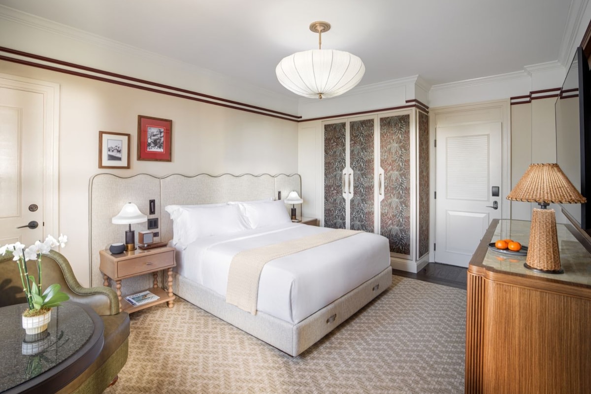 Habitación de hotel con cama, mesitas de noche, escritorio, silla, armario y lámpara.