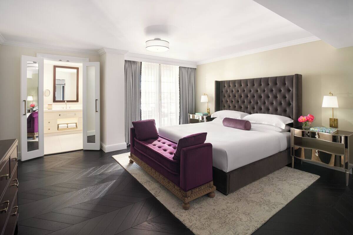 A modern hotel room with a large bed, a sofa, a nightstand, and a bathroom visible through an open door.