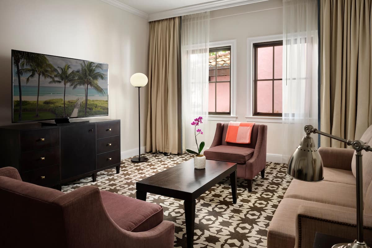 A living room with a flat-screen TV, a sofa, a chair, a coffee table, and a lamp.