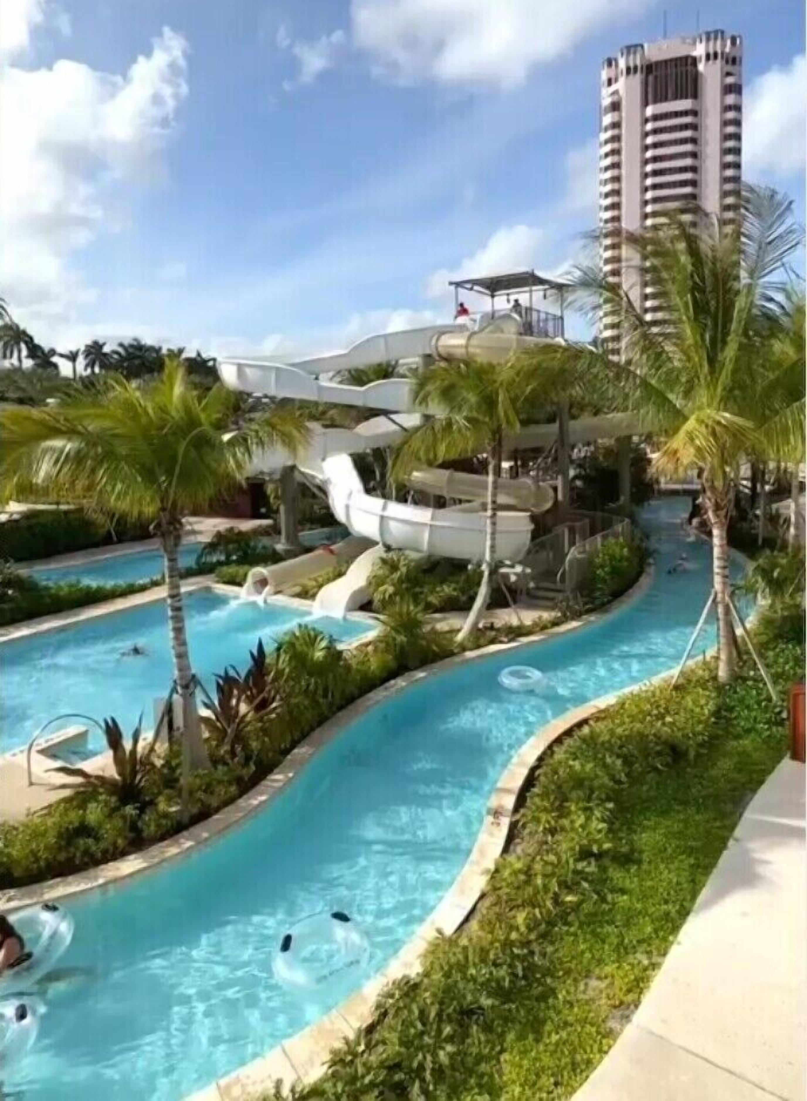 A swimming pool with a water slide and palm trees.