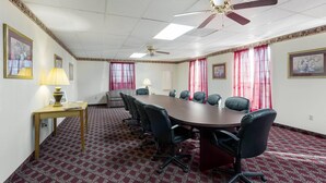 Un salón de conferencias con una gran mesa, sillas, un ventilador de techo y alfombra estampada.