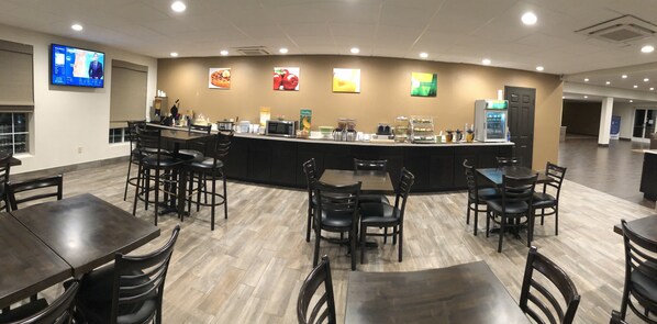 A restaurant with a counter, chairs, tables, and a television screen. - Quality Inn & Suites Paragould (Paragould)