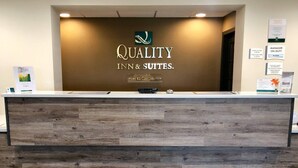 Una recepción con un letrero de Quality Inn & Suites, un cartel con los horarios de registro de entrada y salida, y un aviso indicando que el hotel pertenece a Spirit Business Enterprises.