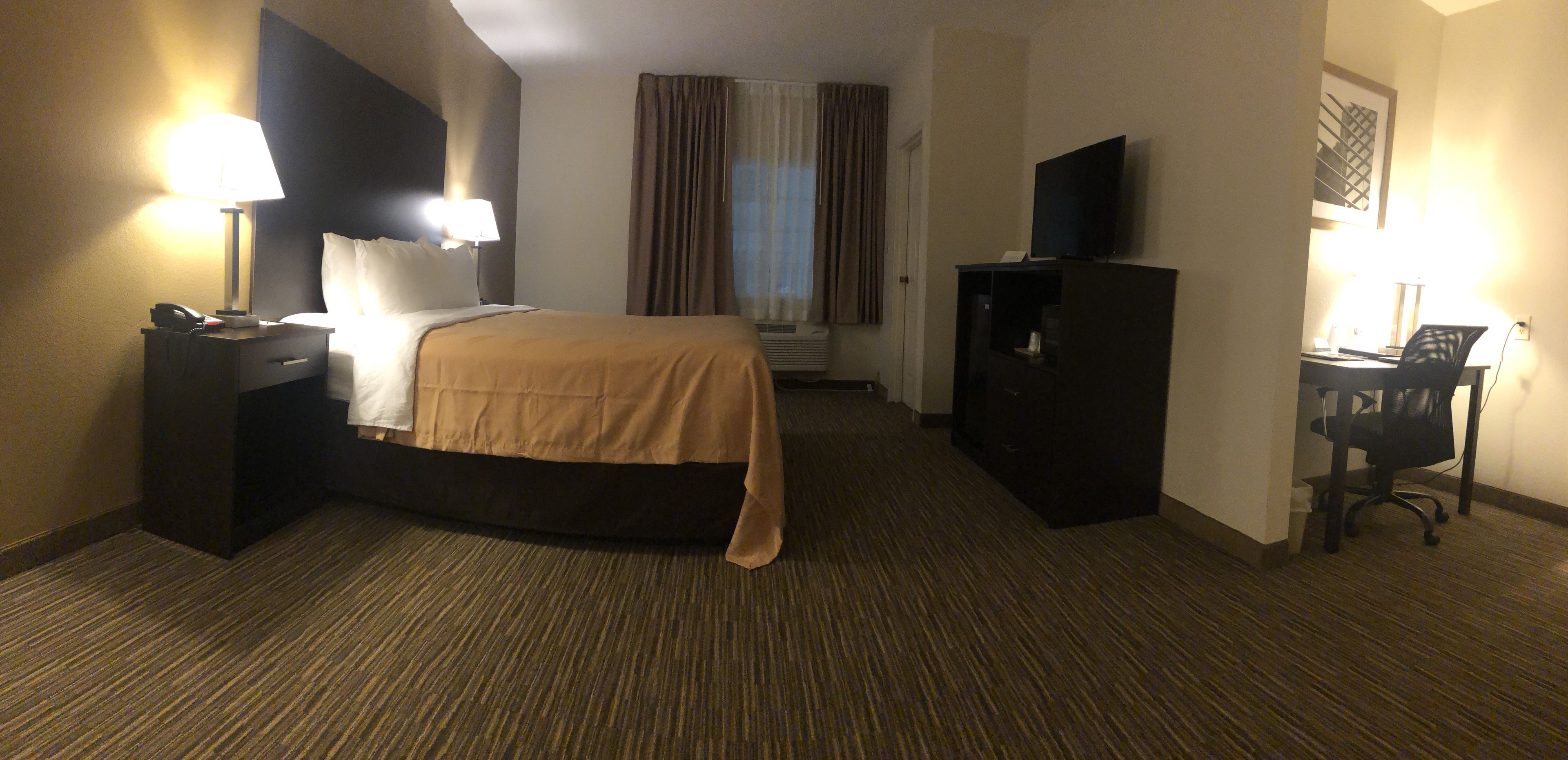 Habitación de hotel con cama, lámparas de noche, escritorio con silla, televisor y ventana con cortinas.